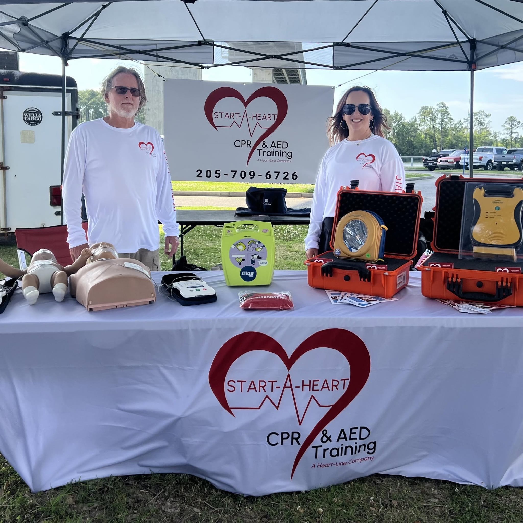 Start-A-Heart team members at a community CPR and AED training booth with manikins and AED units